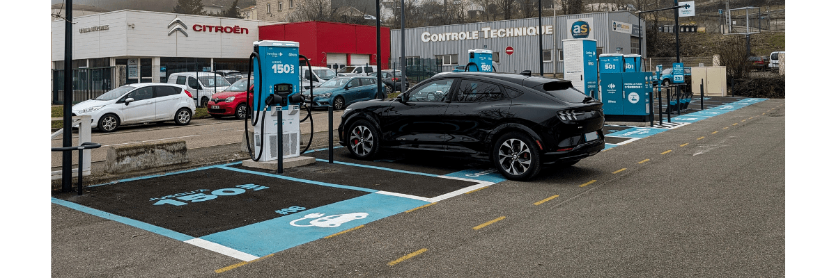 Une voiture électrique - Ford Mustang Mach-E est branchée sur une station de recharge DRIVECO sur le parking d'un Carrefour Market