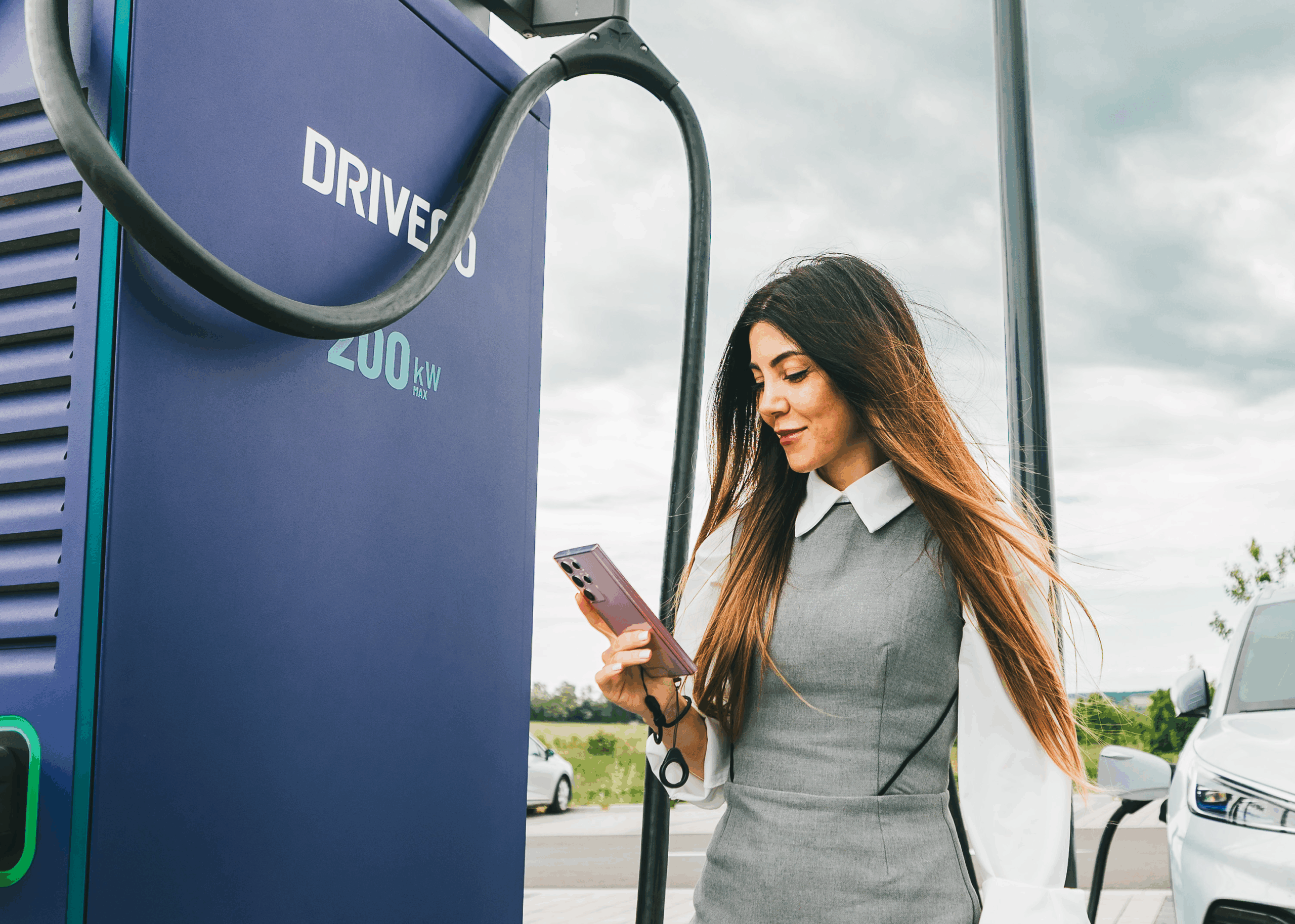 Une utilisatrice de véhicule électrique devant une borne DRIVECO, tient son smartphone en main