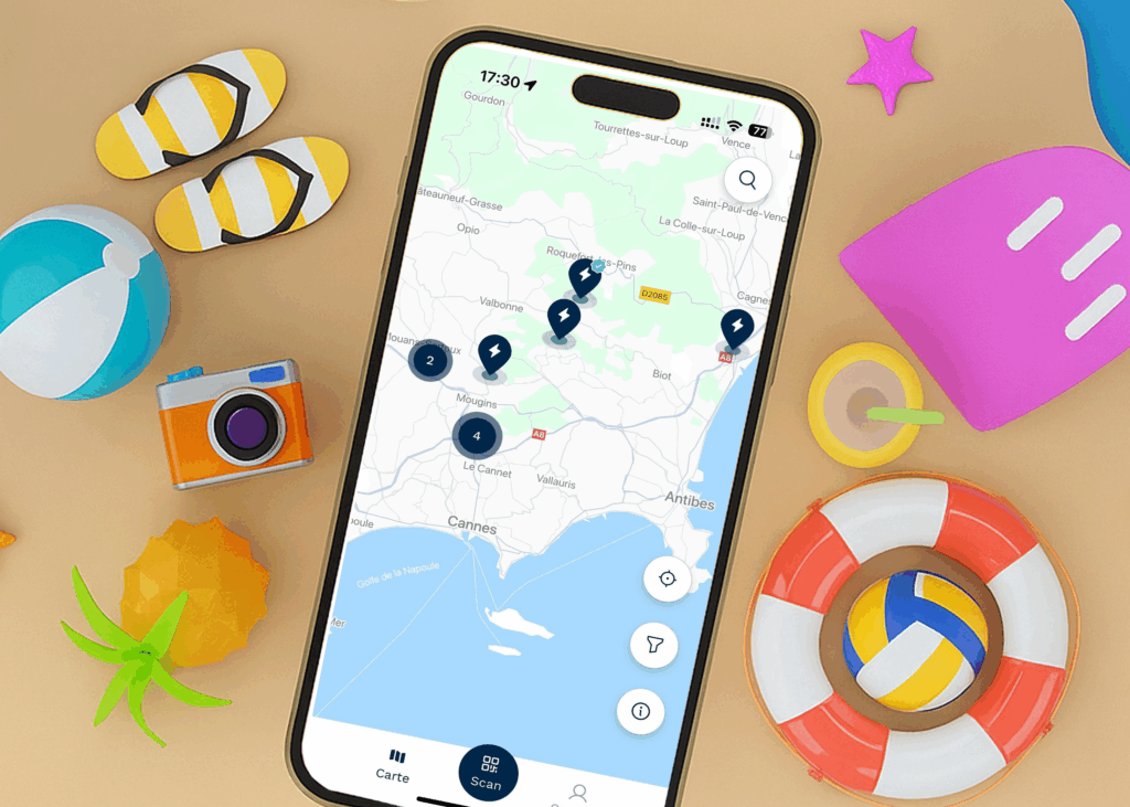 Un smartphone affichant l'app DRIVECO et une carte des stations de recharge autour de la région de Nice, dans un décors de vacances.