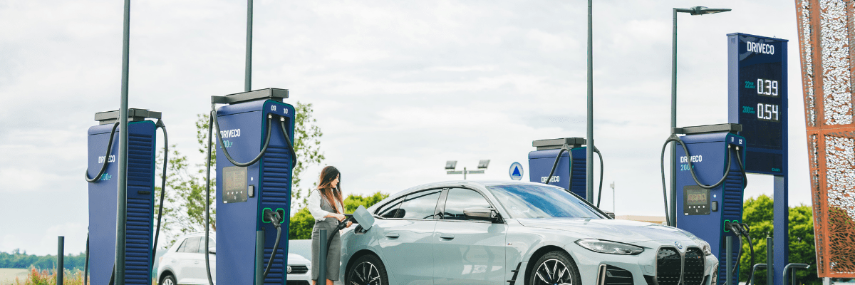Bornes de recharge rapides DRIVECO 200 kW installées sur un parking, une conductrice recharge sa voiture électrique grise BMW i4.