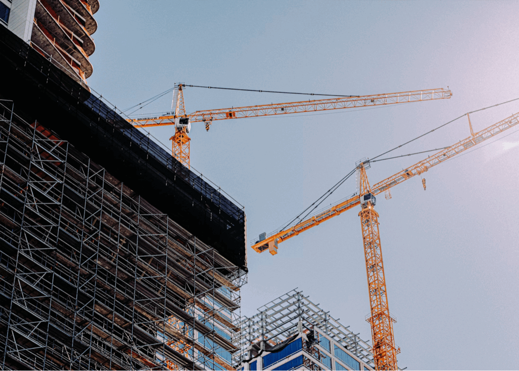 Deux grues de chantier jaunes surplombant un immeuble en construction entouré d’échafaudages métalliques, avec un ciel bleu dégagé en arrière-plan.