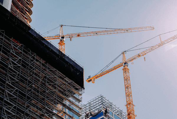 Deux grues de chantier jaunes surplombant un immeuble en construction entouré d’échafaudages métalliques, avec un ciel bleu dégagé en arrière-plan.