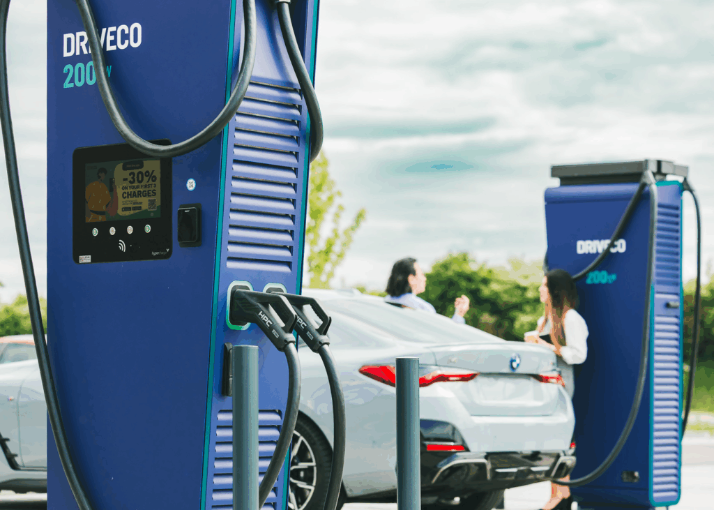 Bornes de recharge rapides DRIVECO 200 kW en fonctionnement, avec un véhicule électrique branché et deux personnes discutant à proximité sur un parking en plein air.
