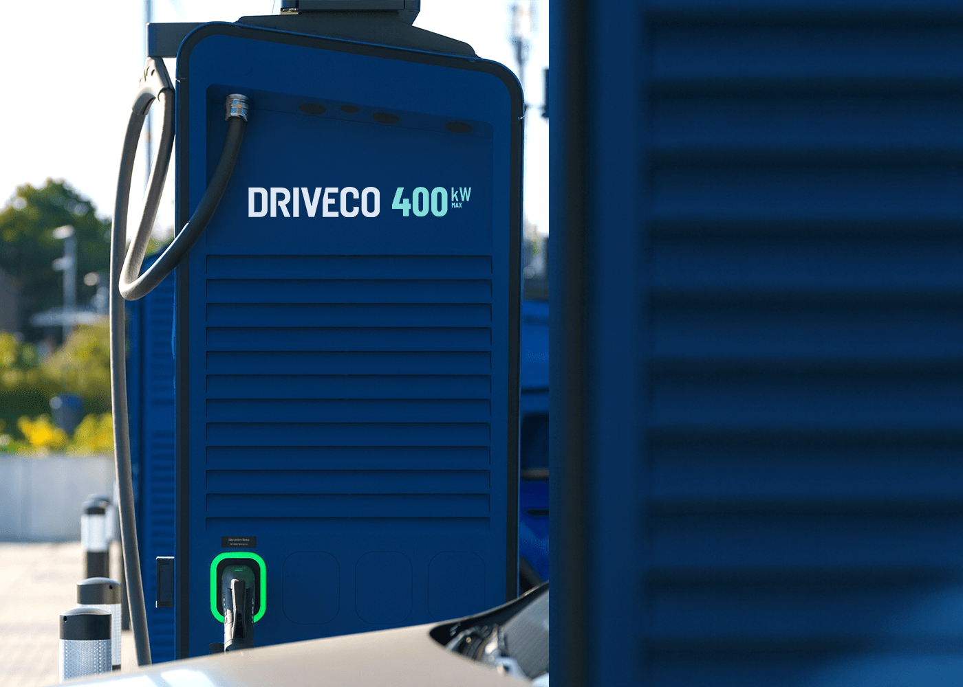Borne de recharge rapide DRIVECO en gros plan, avec connecteur branché à un véhicule électrique sur un parking en extérieur.