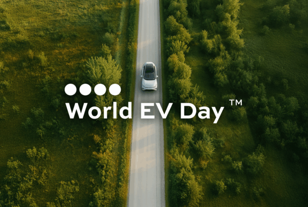 Vue aérienne d’une voiture électrique sur une route bordée d’arbres et de champs, avec le logo World EV Day™ en avant-plan.