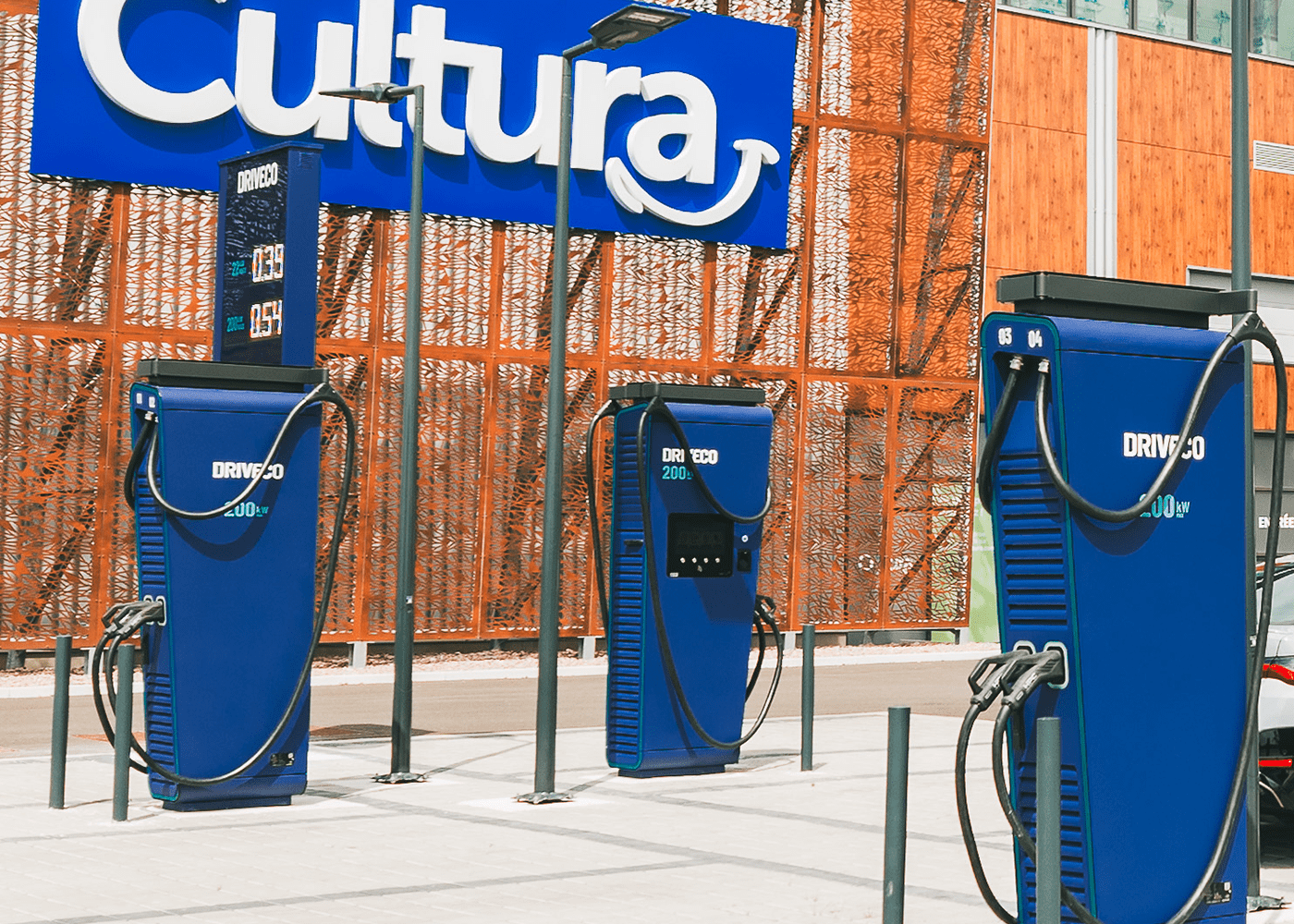Trois bornes de recharge rapide DRIVECO de 200 kW installées sur le parking d’un magasin Cultura, avec affichage des tarifs sur un panneau digital.