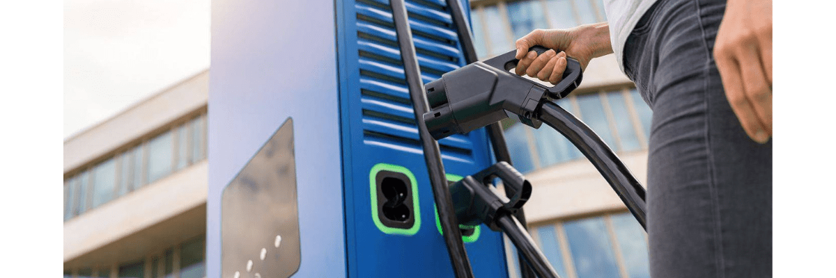Personne branchant un câble sur une borne de recharge pour véhicule électrique en extérieur