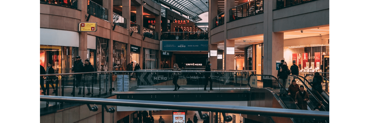 Centre commercial moderne à plusieurs niveaux avec des boutiques éclairées, des escalators et des clients circulant entre les étages.