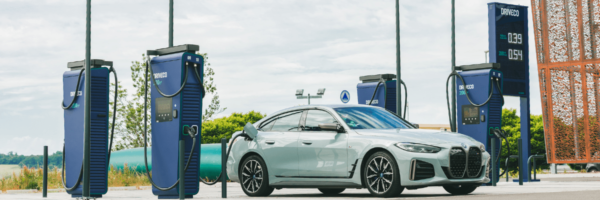 Voiture électrique grise en charge sur une station DRVECO moderne en plein air, avec plusieurs bornes de recharge rapide bleues.