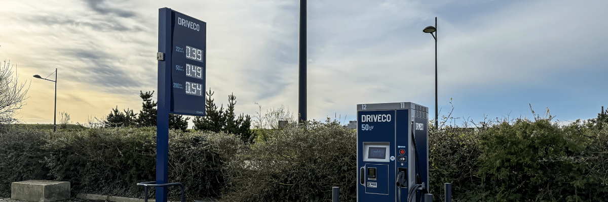 Borne de recharge Driveco de 50 kW installée en extérieur, avec un totem indiquant les tarifs de recharge pour 22 kW, 50 kW et 200 kW, sous un ciel partiellement nuageux.