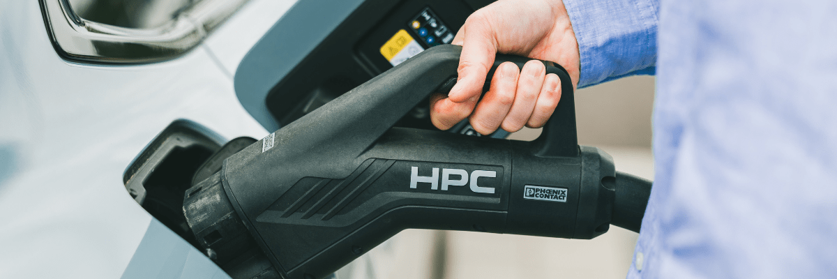 Main branchant un câble de recharge HPC sur une voiture électrique, symbole de la recharge rapide pour entreprises et flottes multi-sites.
