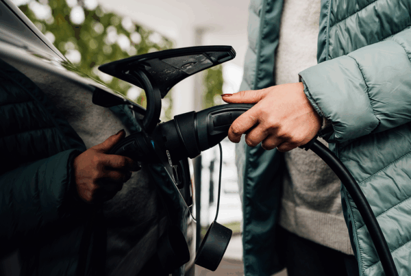 Une personne branche un câble de recharge DRIVECO sur une voiture électrique, portant une doudoune verte.