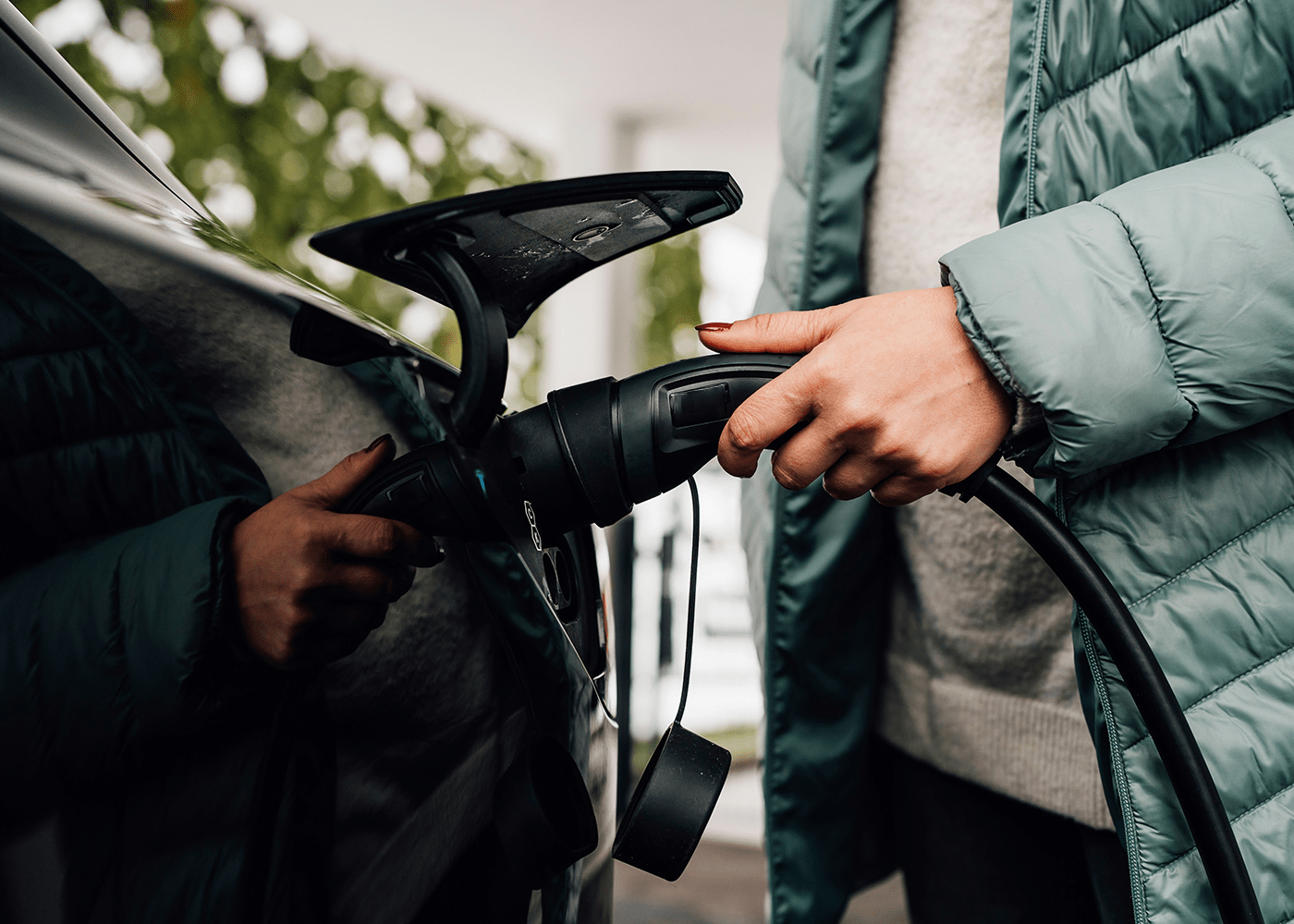 Une personne branche un câble de recharge DRIVECO sur une voiture électrique, portant une doudoune verte.