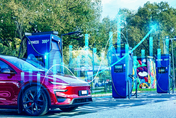 Une voiture électrique rouge est stationnée devant plusieurs bornes de recharge DRIVECO de forte puissance (200 et 300 kW).