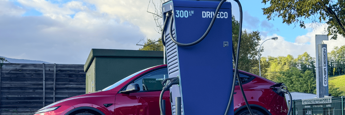 Gros plan sur une borne de recharge ultra-rapide DRIVECO 300 kW avec une Tesla rouge en arrière-plan.