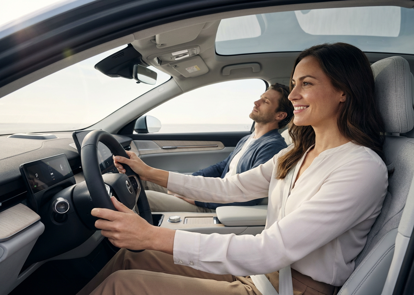 Femme souriante au volant d'une voiture électrique moderne avec toit panoramique, accompagnée d'un passager détendu.