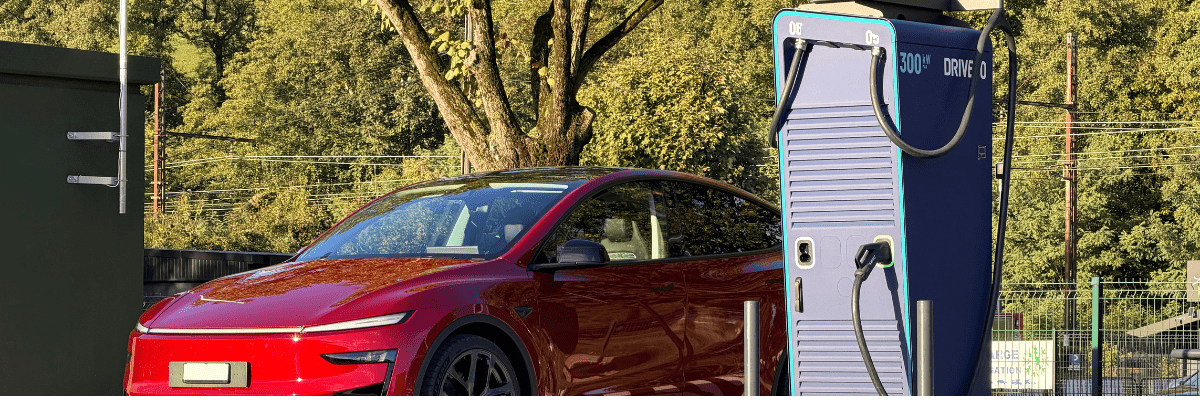 Voiture électrique rouge en train de se recharger sur une borne rapide 300 kW DRIVECO, installée en extérieur dans un environnement verdoyant.