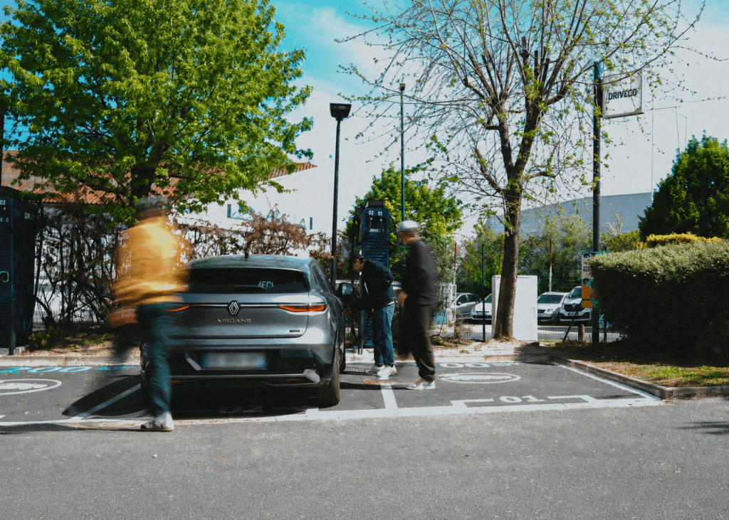 Une voiture électrique garée devant une borne DRIVECO, avec des personnes passant autour du véhicule