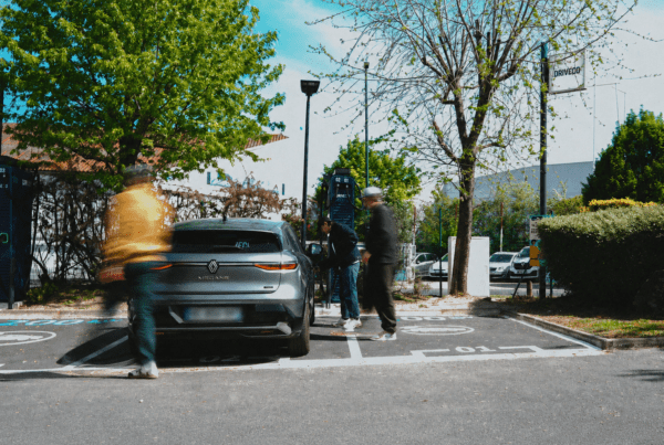 Une voiture électrique garée devant une borne DRIVECO, avec des personnes passant autour du véhicule